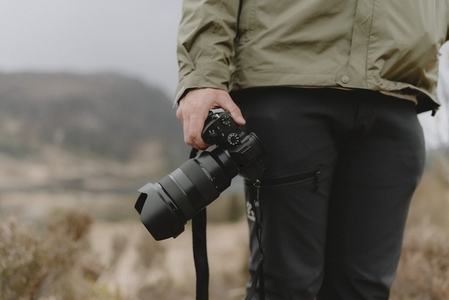 Close up male photographer holding SLR camera in field