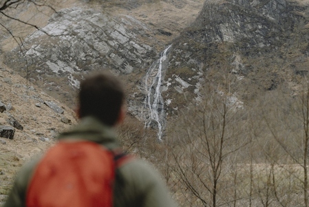 Male hiker watching waterfall on rugged cliff