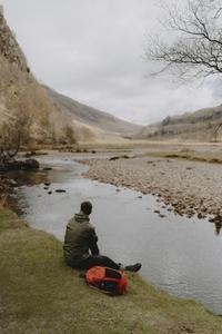 Male hiker resting at tranquil stream in remote landscape