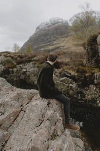 Man sitting on rugged rocks below mountain