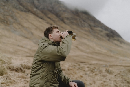 Male hiker drinking from water bottle below cliff