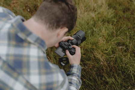 Male photographer looking into viewfinder of SLR camera in grass