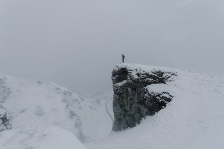 Man standing at edge of mountain rock in snow covered landscape
