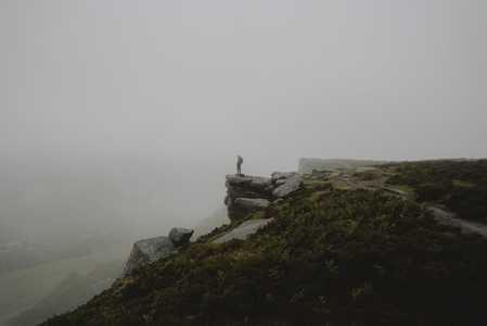 Male hiker at the edge of rocky hilltop in rainy 1