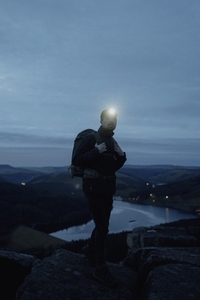 Male hiker with headlamp and backpack on hilltop at night