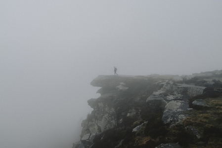 Silhouetted male hiker on rocky cliff in fog