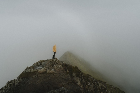 Male hiker on top of rugged rock peak in fog