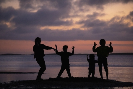 Silhouetted family dancing gesturing on ocean beach at sunset