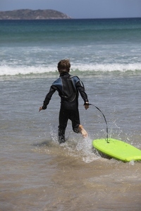 Carefree boy in wet suit running with body board in sunny ocean water