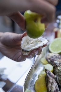 Close up hand squeezing lime over fresh oyster