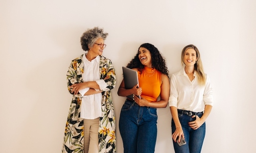 Cheerful businesswomen standing against a wall in an office