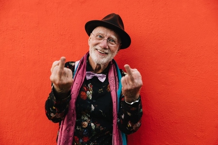 Carefree senior man showing his middle fingers against a red wall