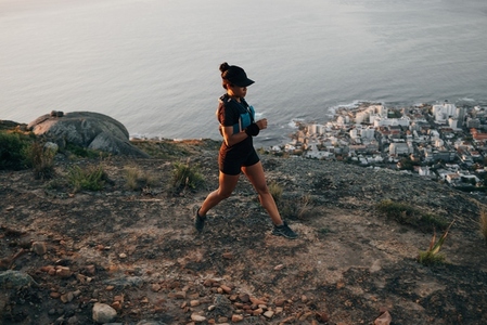 Young woman in sportswear running on mountain at sunset