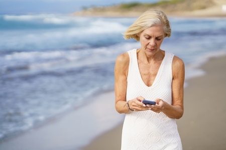 Mature female walking on the beach using a smartphone