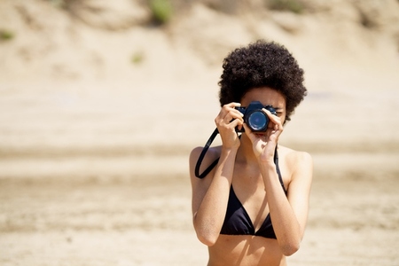 Black woman in bikini taking photo on beach