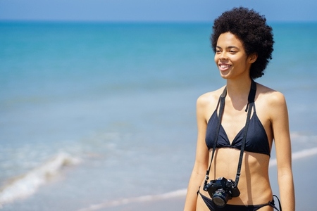 Smiling black woman with photo camera near sea