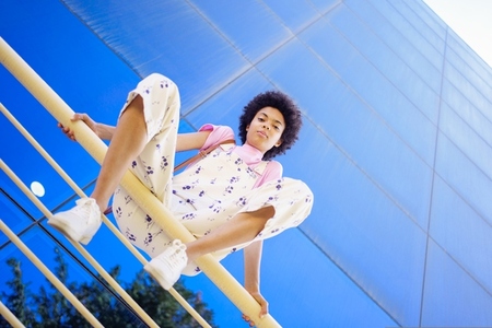 African American woman in casual clothes  sitting on a railing of a modern building