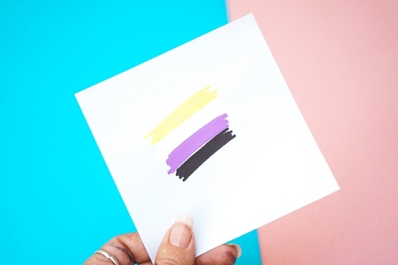 Hand holding a paper with non binary flag drawing in it