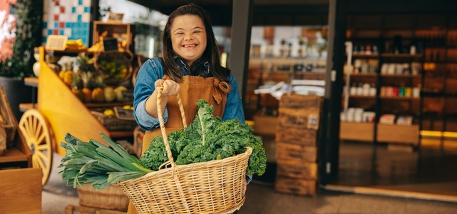 Grocery store employee with down syndrome holding a basket of fresh vegetables