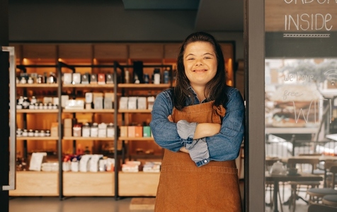 Cheerful woman with Down syndrome standing at the door of a shop