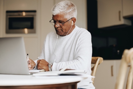 Senior businessman writing in a notebook while working from home