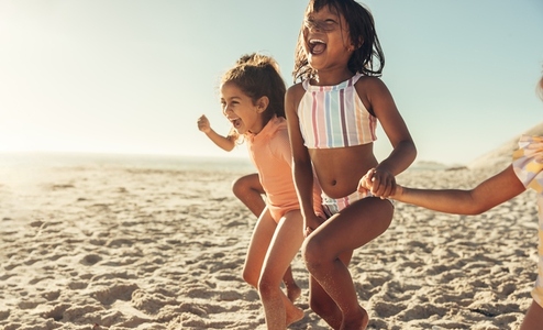 Excited little girls running together at the beach