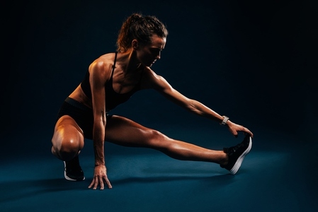 Muscular woman stretching her leg on black background