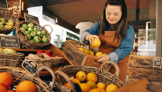 Woman with Down syndrome restocking fresh fruits in a shop