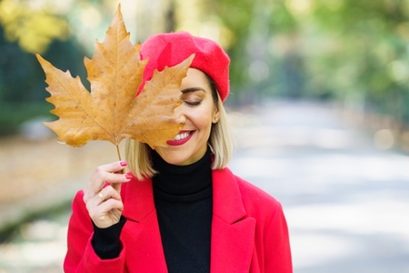 Smiling woman covering face with dry leaf