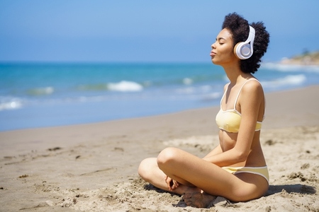 Relaxed ethnic lady listening to music and meditating on beach