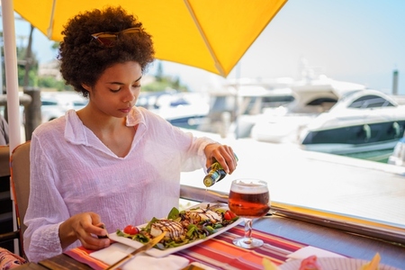 Black woman adding oil to dish in street restaurant