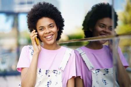 Cheerful black woman talking on smartphone near building