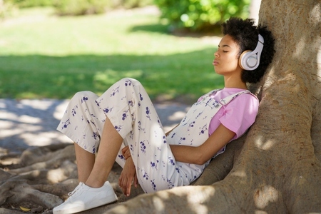 Black woman listening to music near tree
