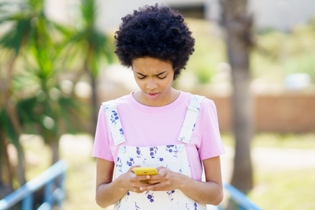 Focused black woman surfing smartphone on street