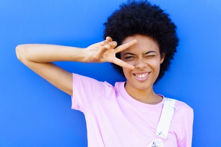 Cheerful black woman making peace sign near wall