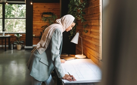 Thoughtful Muslim designer working with blueprints in an office