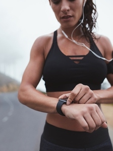 Fit woman adjusting smartwatch while exercising outdoors