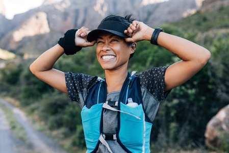 Laughing woman hiker holding cap enjoying the view  Young woman in sports wear in wild terrain
