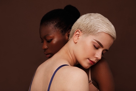 Two young women with different skin color standing together  Females put their heads on each others shoulders with closed eyes