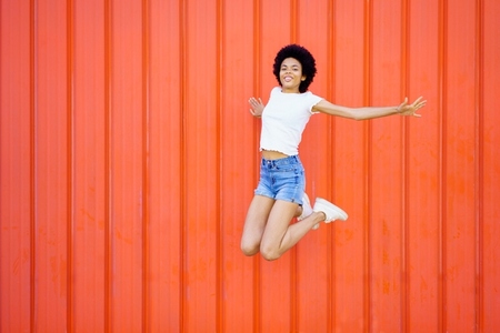 Black girl jumping with raised arms against a red urban wall