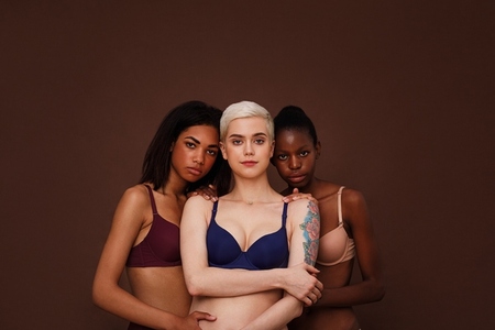 Three women of different skin color standing together  Group of young female in lingerie against backdrop