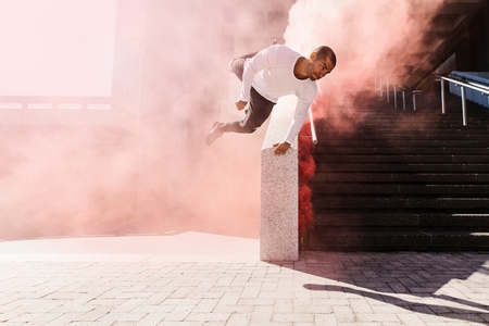 Young man practicing parkour in an urban space with smoke grenade