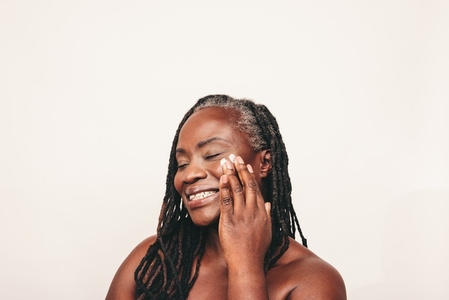 Happy mature woman applying moisturizing cream on her face