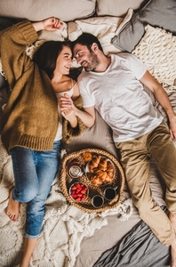 Happy smiling couple having breakfast in bed and holding hands