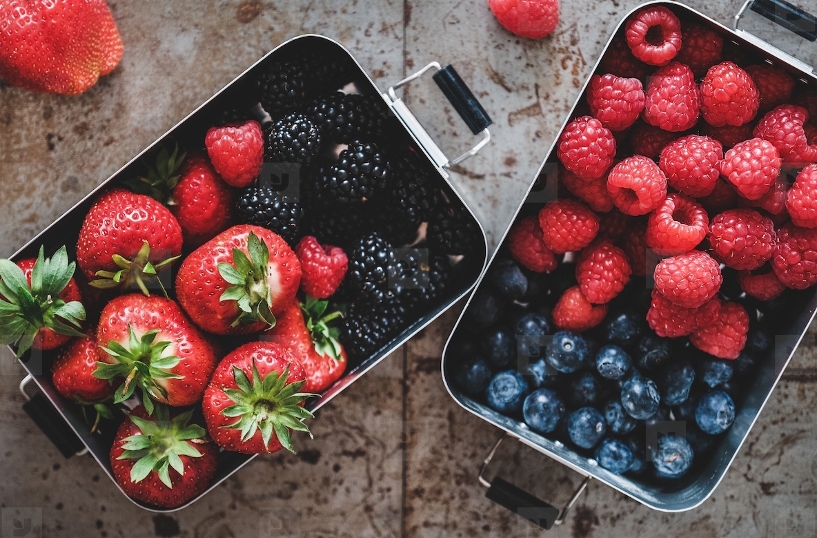 Flat lay of fresh berries in metal lunchboxes over grey background