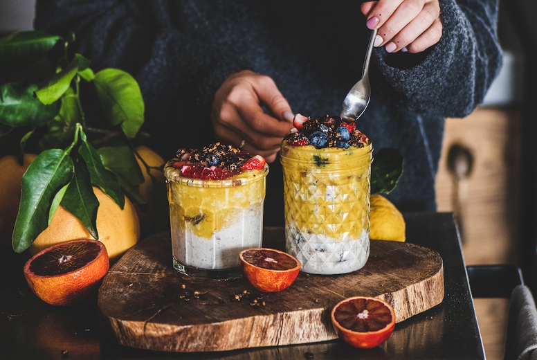 Woman eating muesli with mango smoothie and granola with spoon