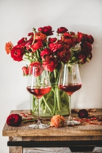 Rose wine in glasses and red flowers over wooden table