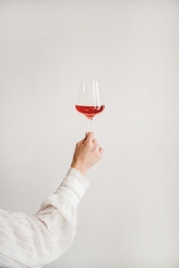 Womans hand holding glass of rose wine over white wall
