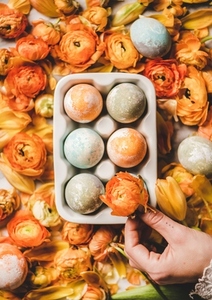Womans hand holding flower over dyed Easter eggs and petals
