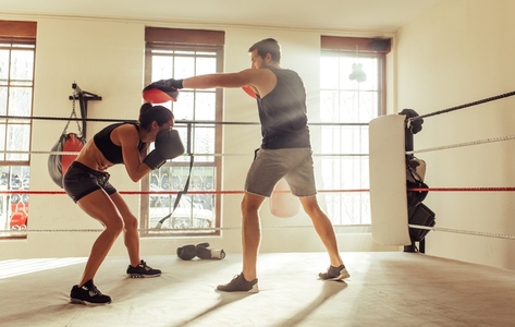Young boxer ducking a strike from her personal trainer in a boxing ring